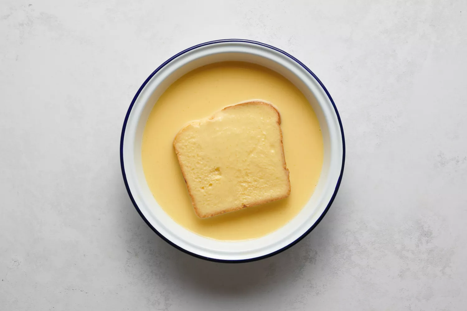 Um pedaço de pão mergulhando na mistura de ovos e leite batidos