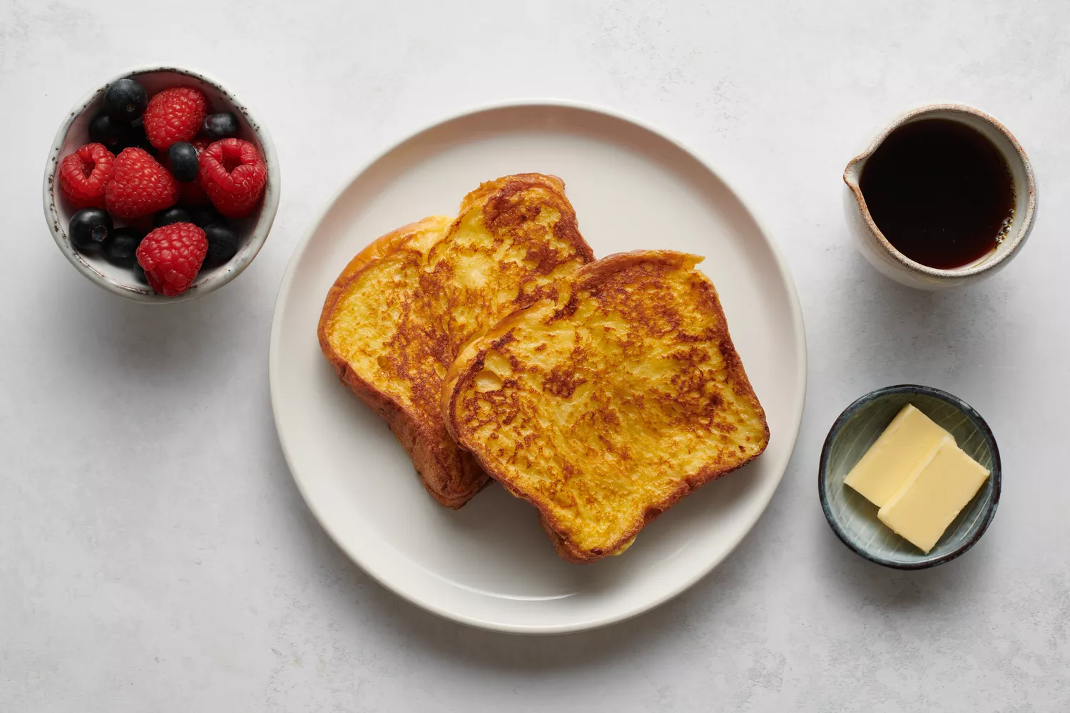 Um prato de torrada francesa servido com manteiga, xarope e frutas vermelhas