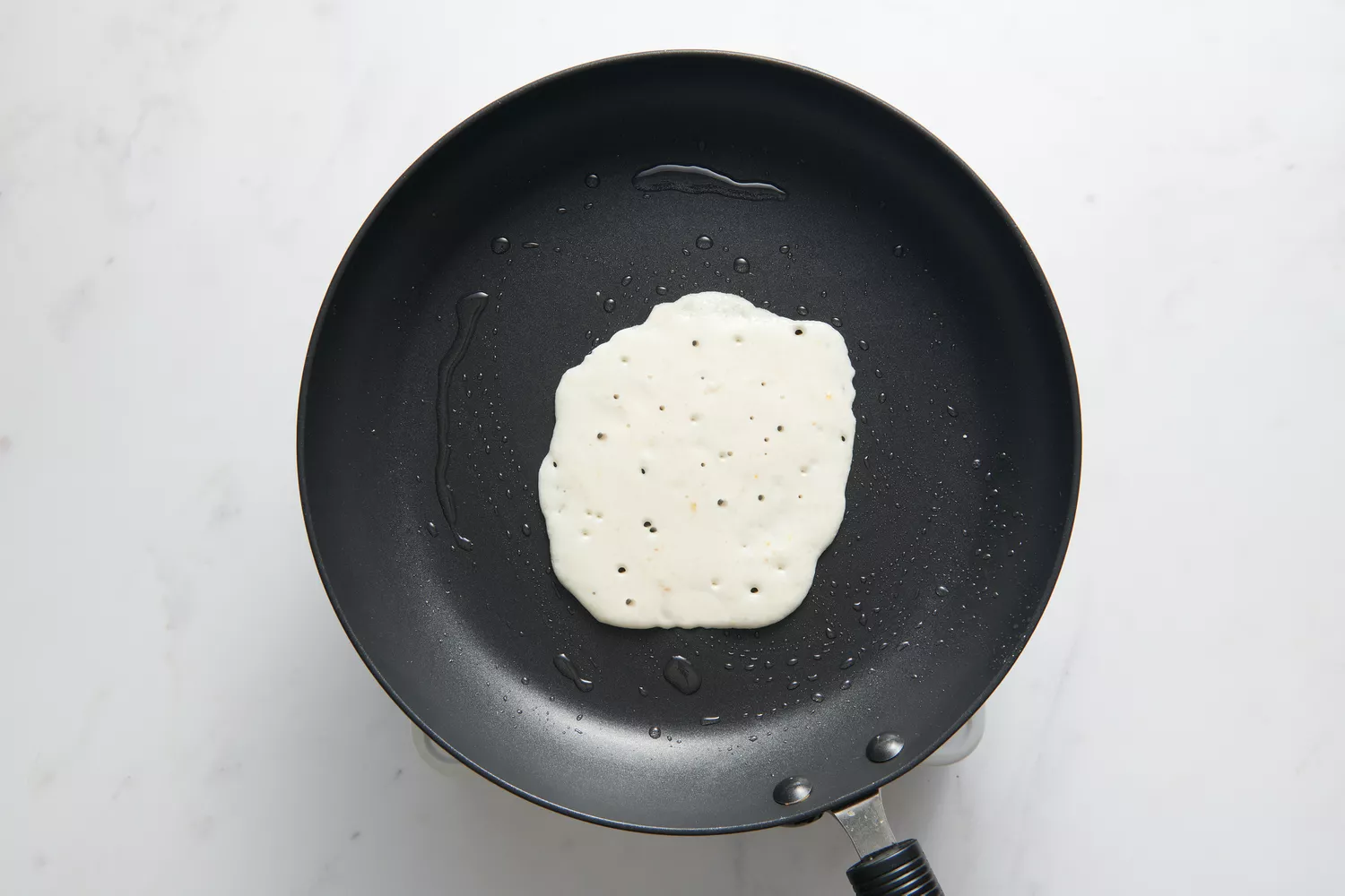 Uma pequena porção da massa derramada no meio da frigideira antiaderente untada