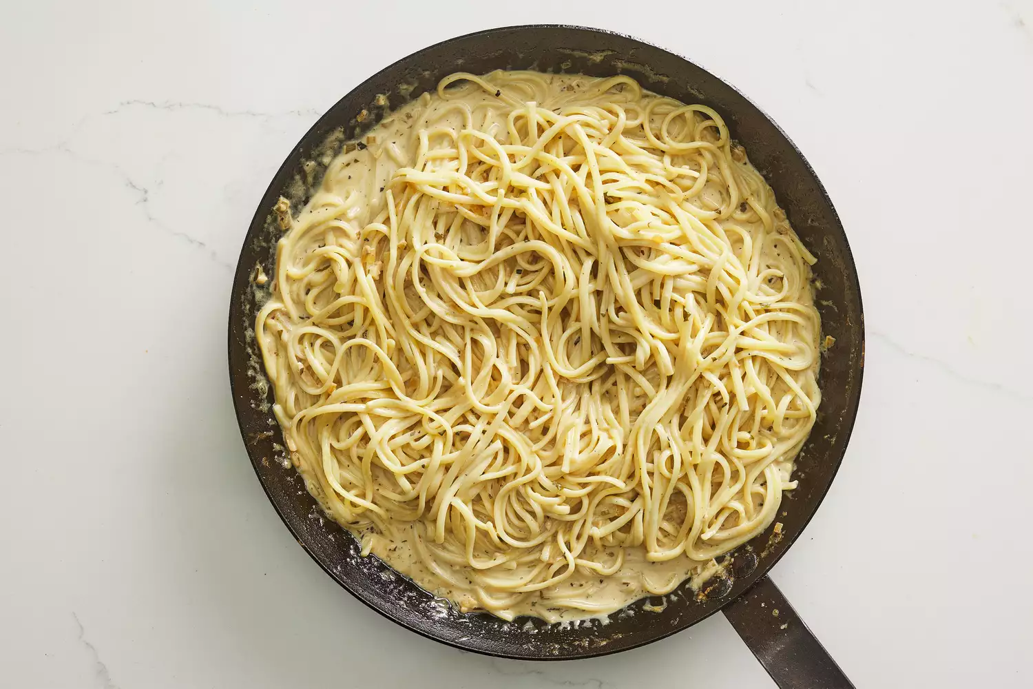Uma frigideira com fettuccine cozido misturado em um molho cremoso de Dijon e parmesão