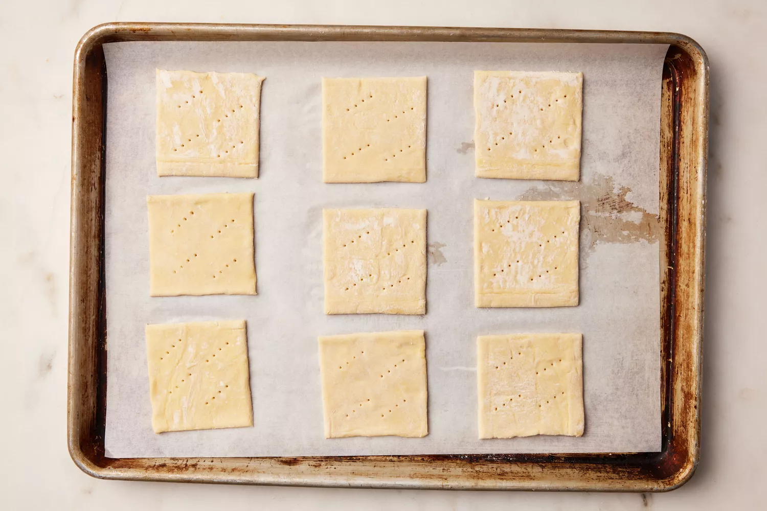 A parchment paper-lined baking sheet with nine squares of puff pastry, pricked with a fork