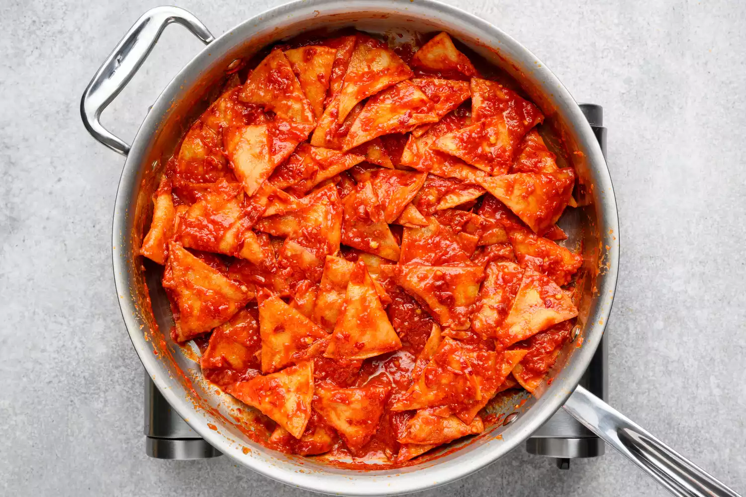 Uma panela de chips de tortilla fritos misturados em um molho de tomate e chile
