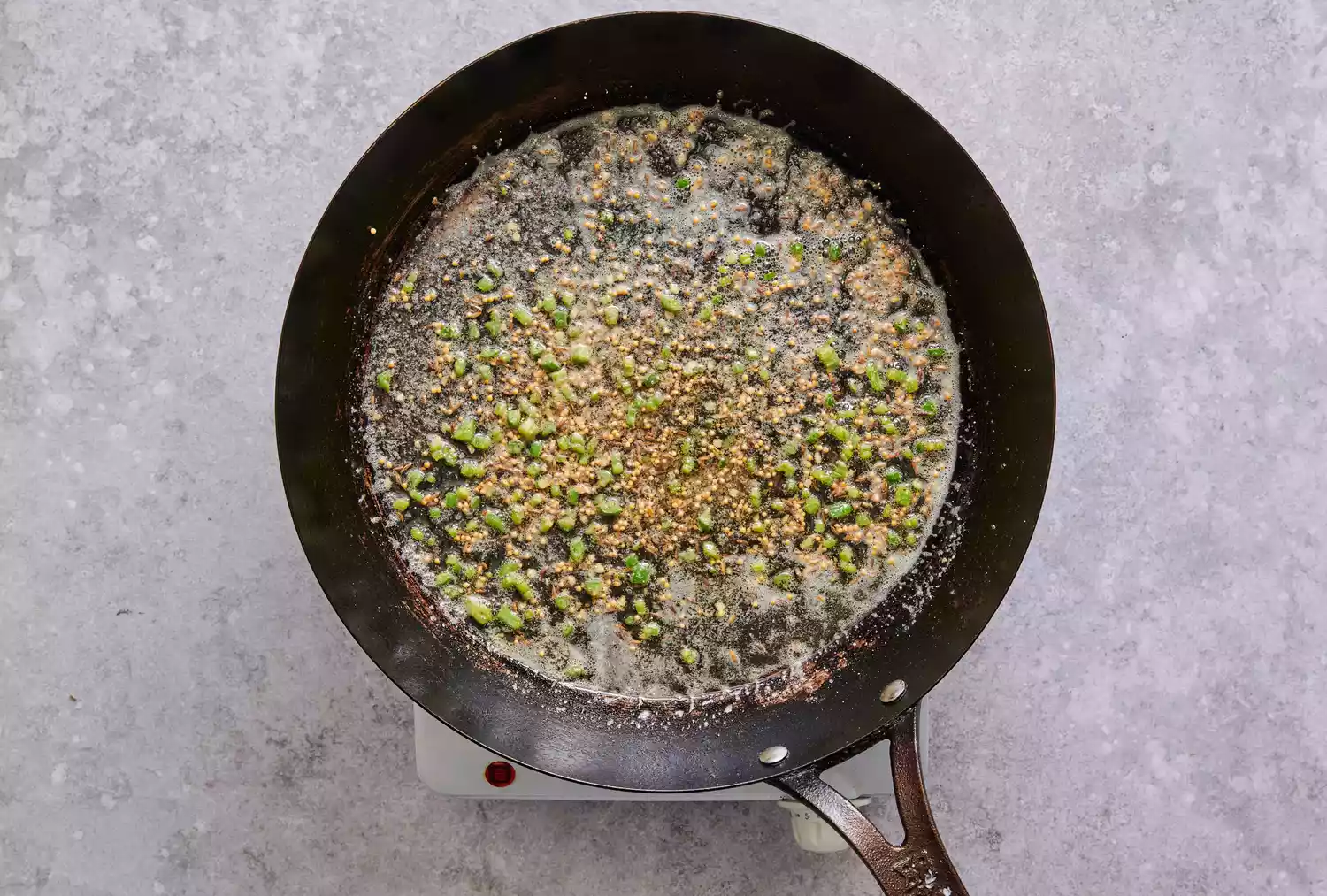 Uma frigideira grande com sementes de mostarda, sementes de cominho, asafoetida e pimenta verde cozinhando em ghee