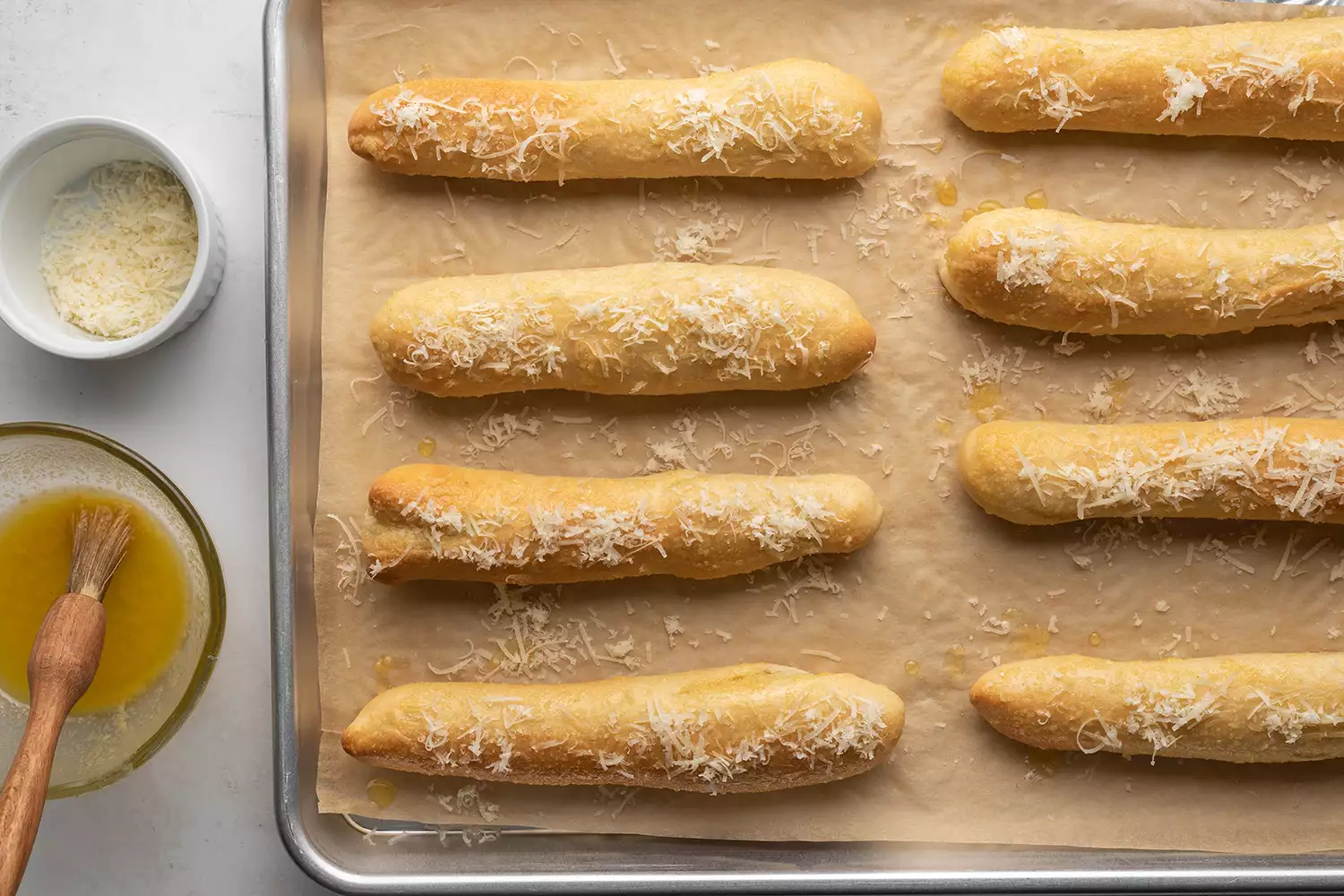 Copycat Crazy Bread em uma assadeira forrada com papel manteiga, manteiga de alho e queijo em tigelas